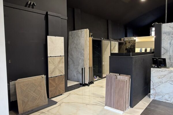 Showroom displaying tile and marble samples on display panels against dark walls with overhead lighting. It features large marble floor tiles and sample boards on stands.