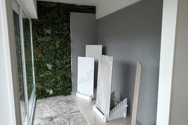 Showroom interior with a green plant wall, marble floor tiles, and display samples leaning against the gray wall for selection.