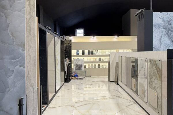 Interior of a tile showroom with marble-style floor tiles, wall sample displays, and bright ceiling lights.