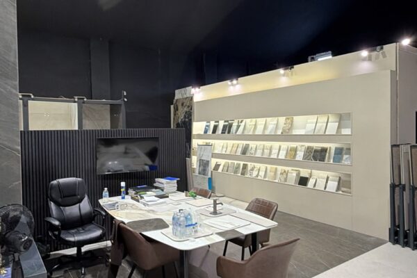 Showroom interior with a meeting table, brown chairs, and wall shelves displaying tile or material samples along a white wall.