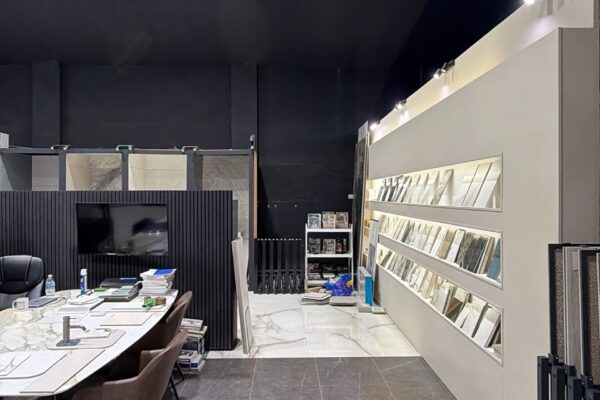 Interior of a modern showroom with a long white conference table on the left and display shelves of samples along the right wall, marble floors and a dark ceiling.