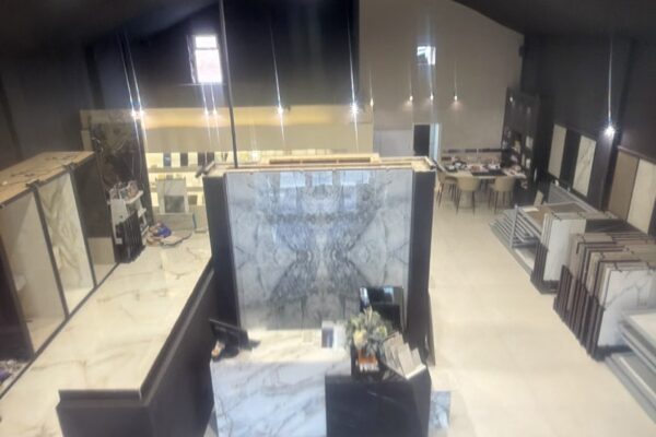 Interior of a tile and stone showroom with marble slabs on display stands and floor samples, brightly lit by ceiling spotlights.