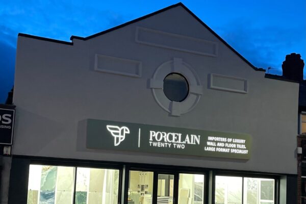Tile showroom storefront at dusk with a circular decorative facade and large glass windows displaying tile samples; sign reads 'Porcelain Twenty Two'