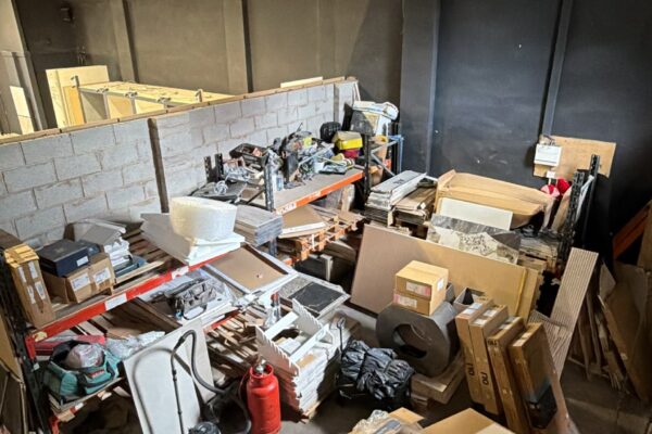 Messy indoor storage/workshop with shelves, boxes, and scattered tools and materials.